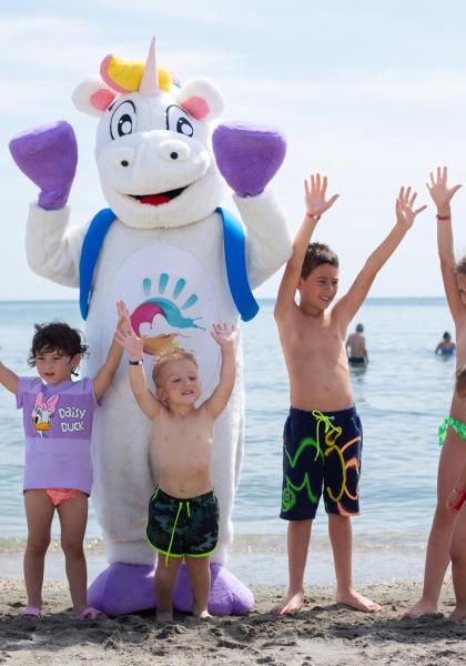 Kinder und ein Einhorn am Strand heben fröhlich die Hände.