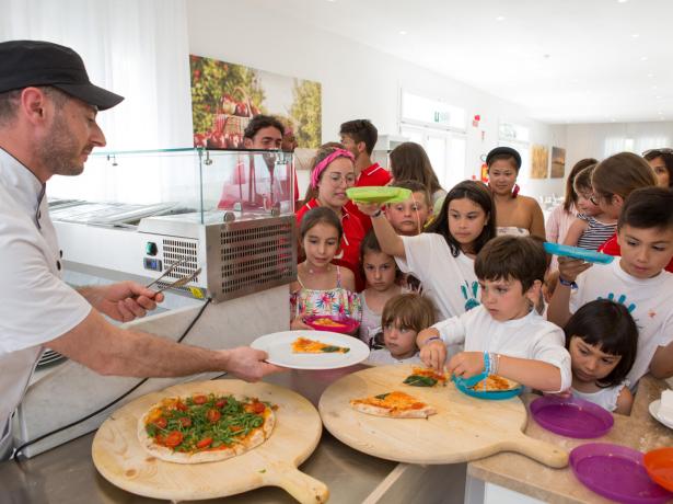 Enfants en file pour la pizza, servis par un cuisinier.