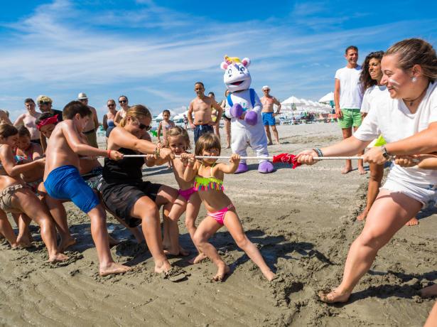 Tir à la corde sur la plage avec spectateurs et mascotte.