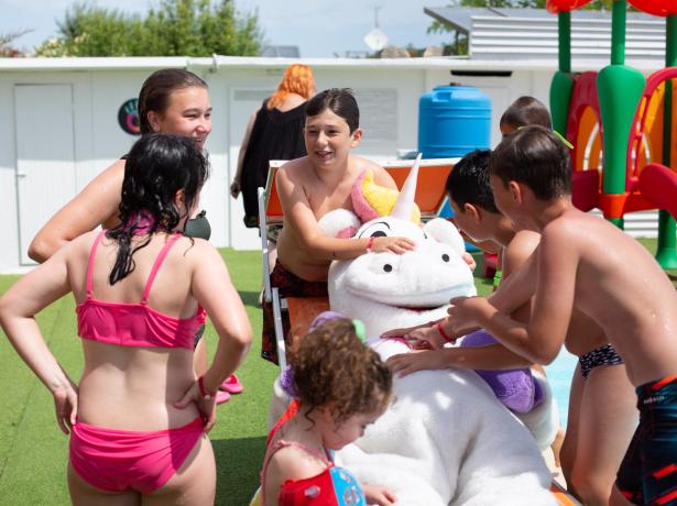 Des enfants jouent avec un costume de licorne près de la piscine.