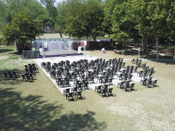 Outdoor area with chairs and stage, surrounded by trees.