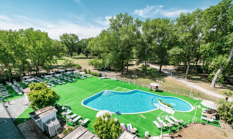 Outdoor pool surrounded by greenery and sunbeds, nestled in nature.