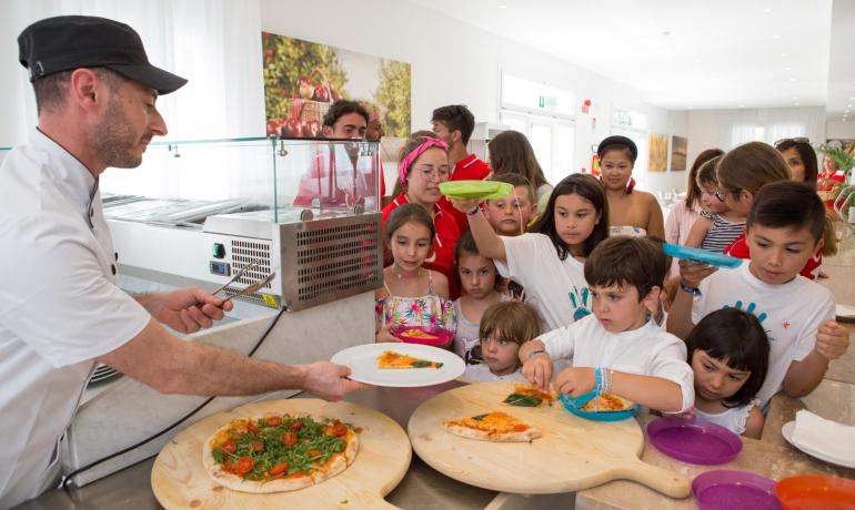Bambini in fila per la pizza, serviti da un cuoco.