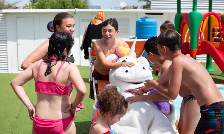 Kinder spielen mit einem Einhornkostüm am Pool.