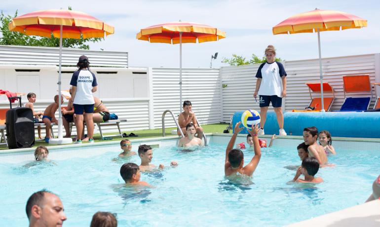 Bambini giocano in piscina sotto la supervisione degli animatori.