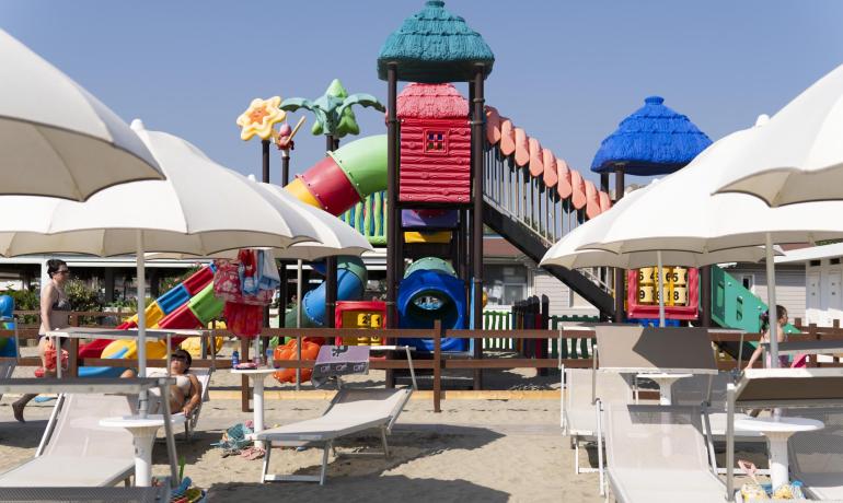 Plage avec aire de jeux colorée et parasols blancs.