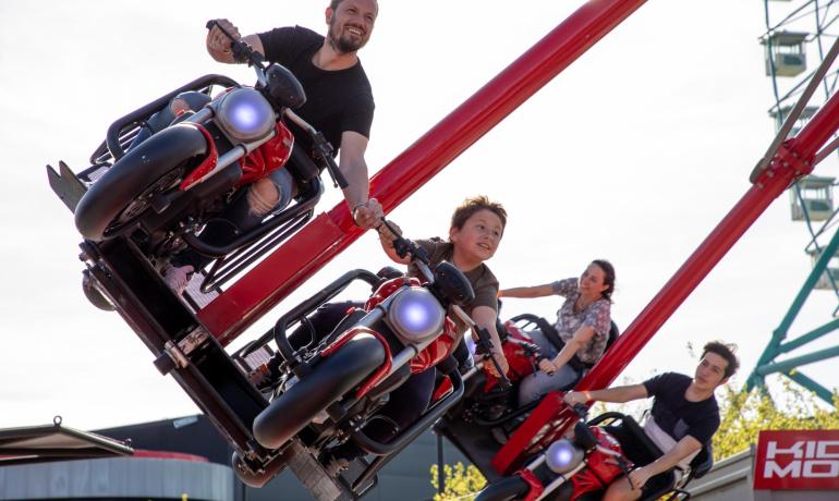 Persone sorridenti su una giostra di moto in movimento, emozione e adrenalina.