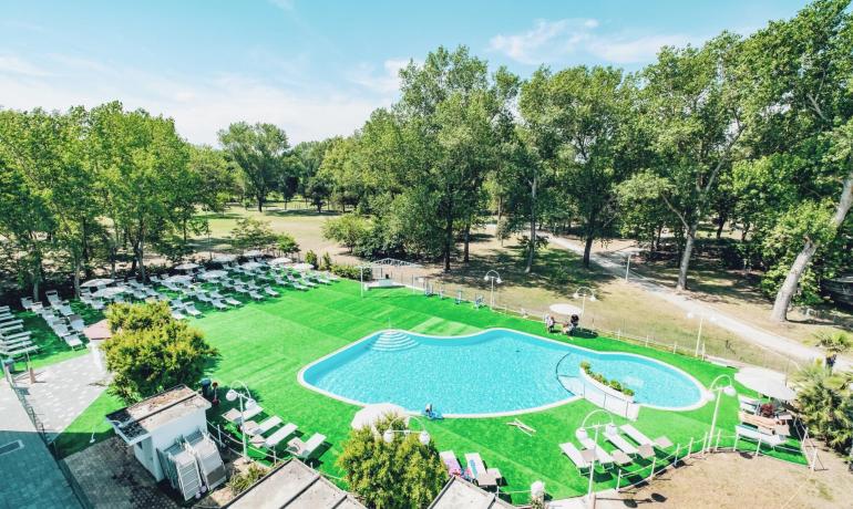 Piscina all'aperto con lettini, circondata da alberi e prato verde.