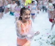 Fille joyeuse joue dans la mousse, entourée de rires et de plaisir estival.