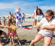 Persone festeggiano in spiaggia lanciando polvere colorata, creando un'atmosfera vivace e gioiosa.