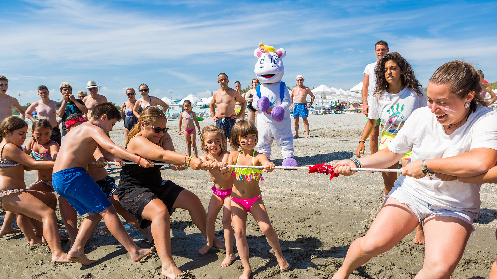 Famiglia cammina sulla spiaggia, tra ombrelloni e sdraio, verso il mare.