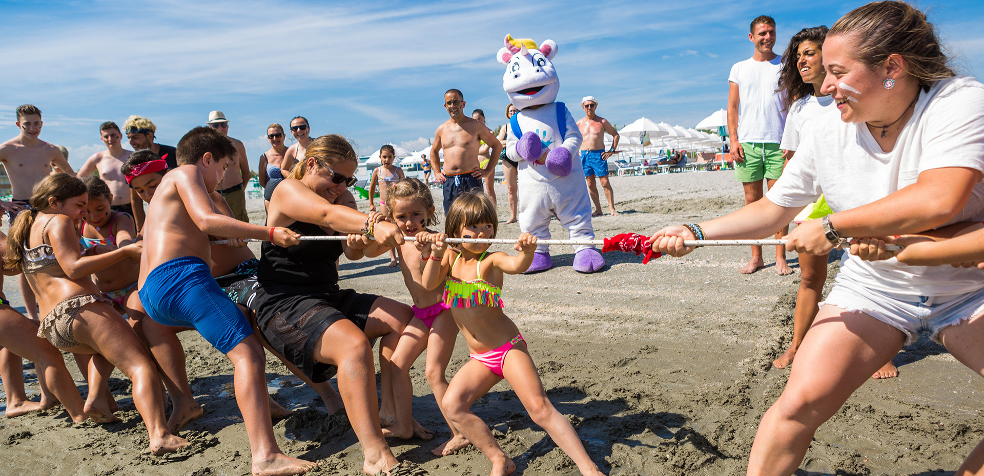 Kinder und Erwachsene spielen Tauziehen am Strand, Lächeln und Freude.