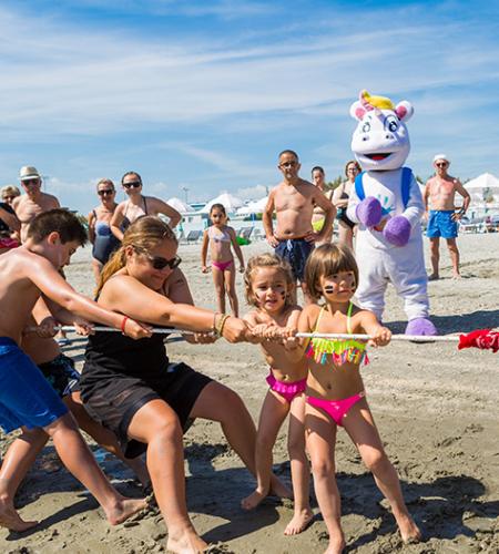 Bambino seduto al tavolo con colori, accompagnato da un adulto sorridente.