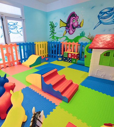 Area giochi per bambini con scivolo giallo e sedie colorate.