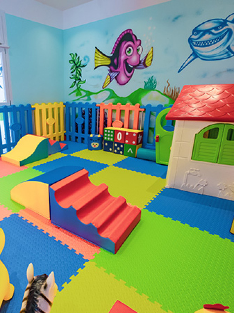 Area giochi per bambini con scivolo giallo e sedie colorate.