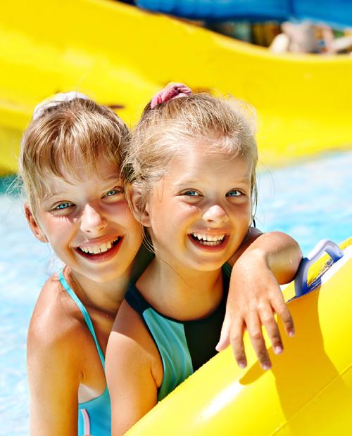 Due bambine sorridenti giocano felici in piscina con un grande salvagente colorato.