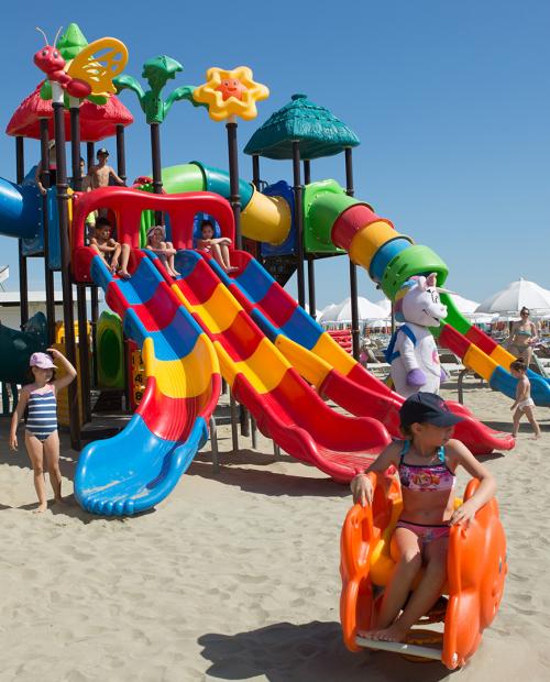 Papà e figlia sorridenti giocano sulla spiaggia con secchiello e paletta.
