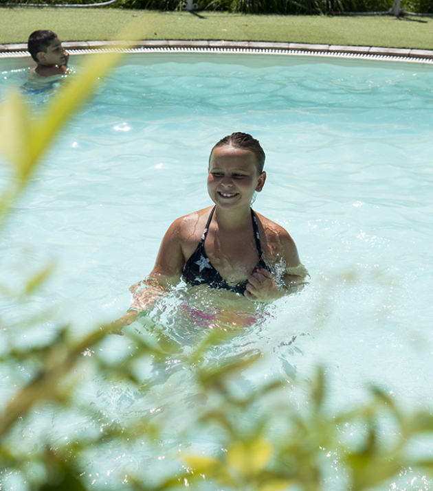 Bambino in piscina con braccioli arancioni, seduto vicino all'acqua.