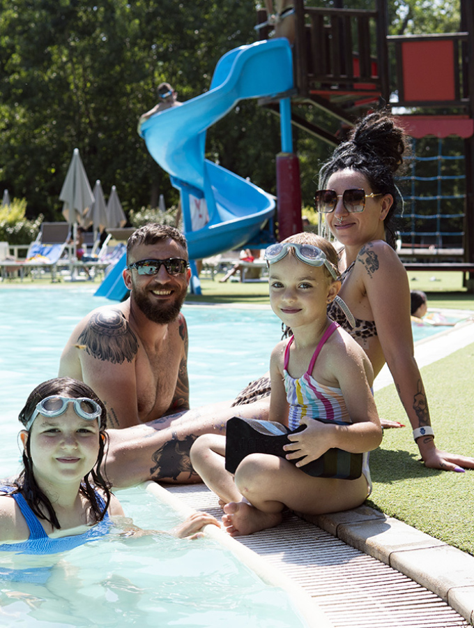 Donna con bambino passeggia tra ombrelloni arancioni su una spiaggia assolata.