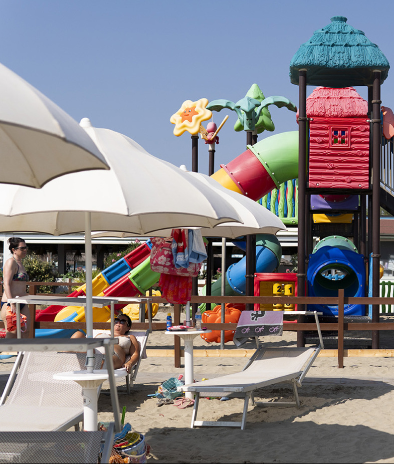 Ragazzo sistema ombrellone su spiaggia deserta, indossando occhiali da sole e maglietta blu.